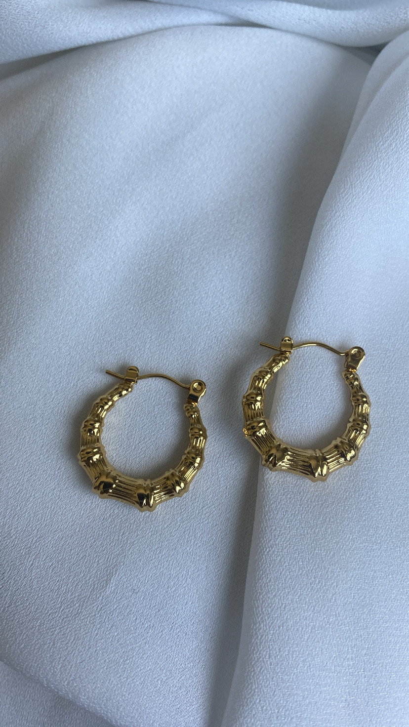 Brincos argola dourados com textura de bambu sobre tecido branco