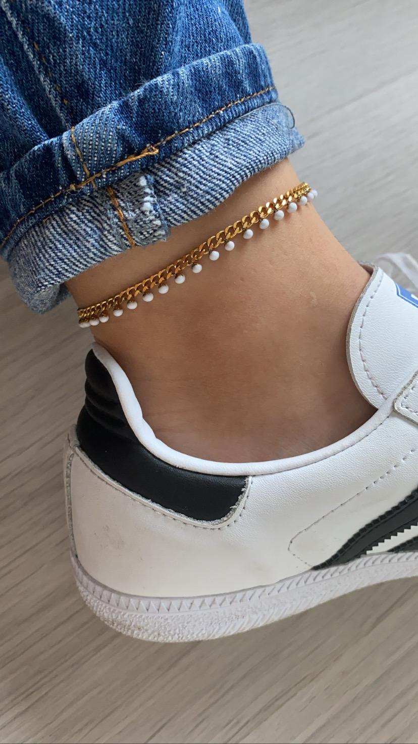 Tornozeleira dourada com contas brancas no tornozelo, calça de ganga e sapatilha branca