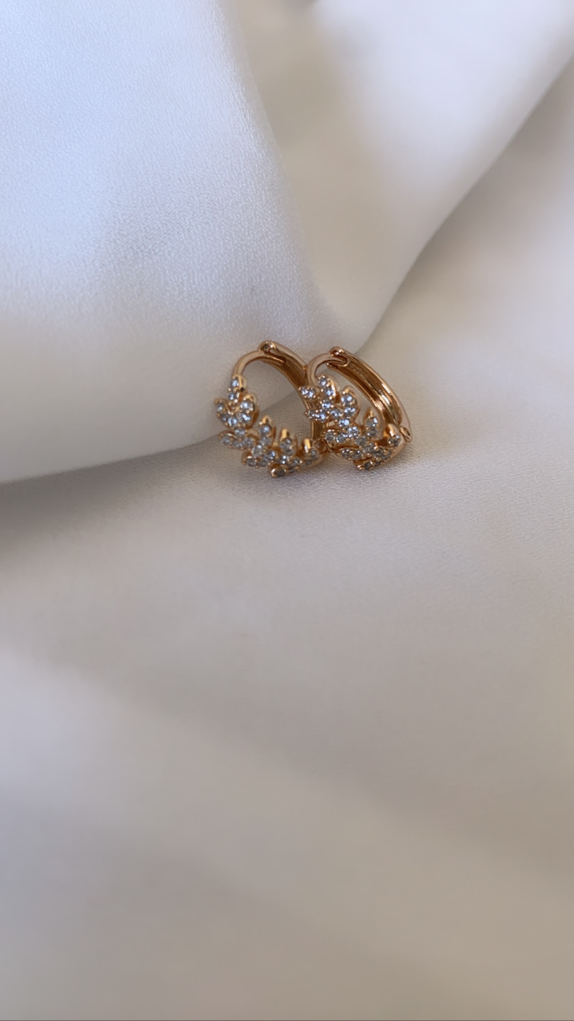 Brincos dourados com pedras transparentes sobre tecido branco