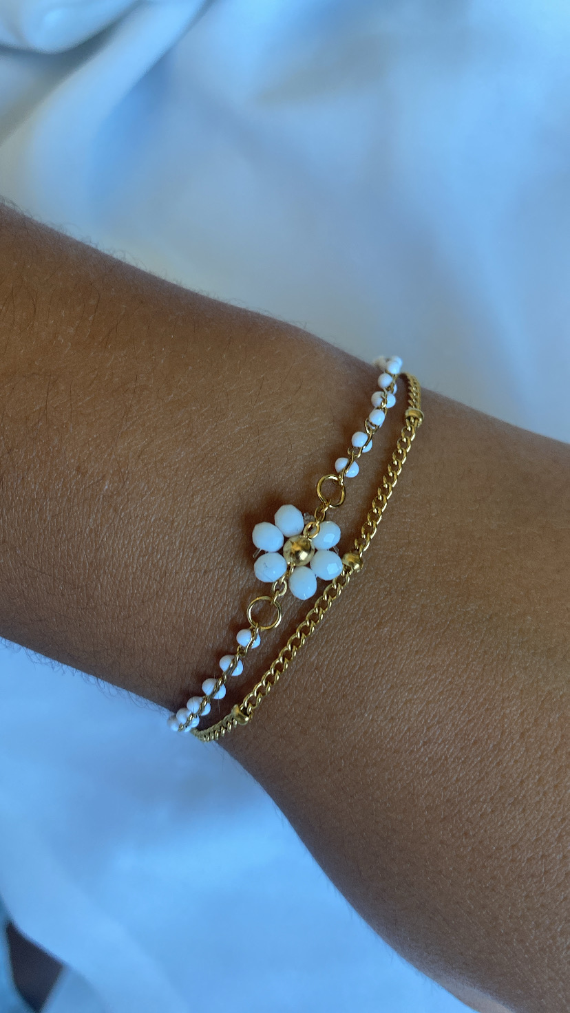 Pulseira dourada com pedras brancas em formato de flor num pulso.