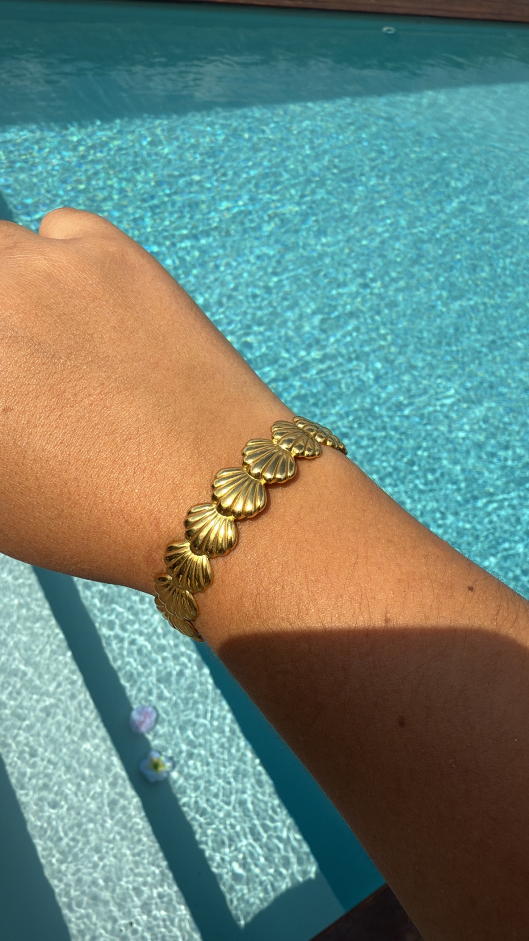 Pulseira dourada com desenhos de conchas num braço junto à piscina
