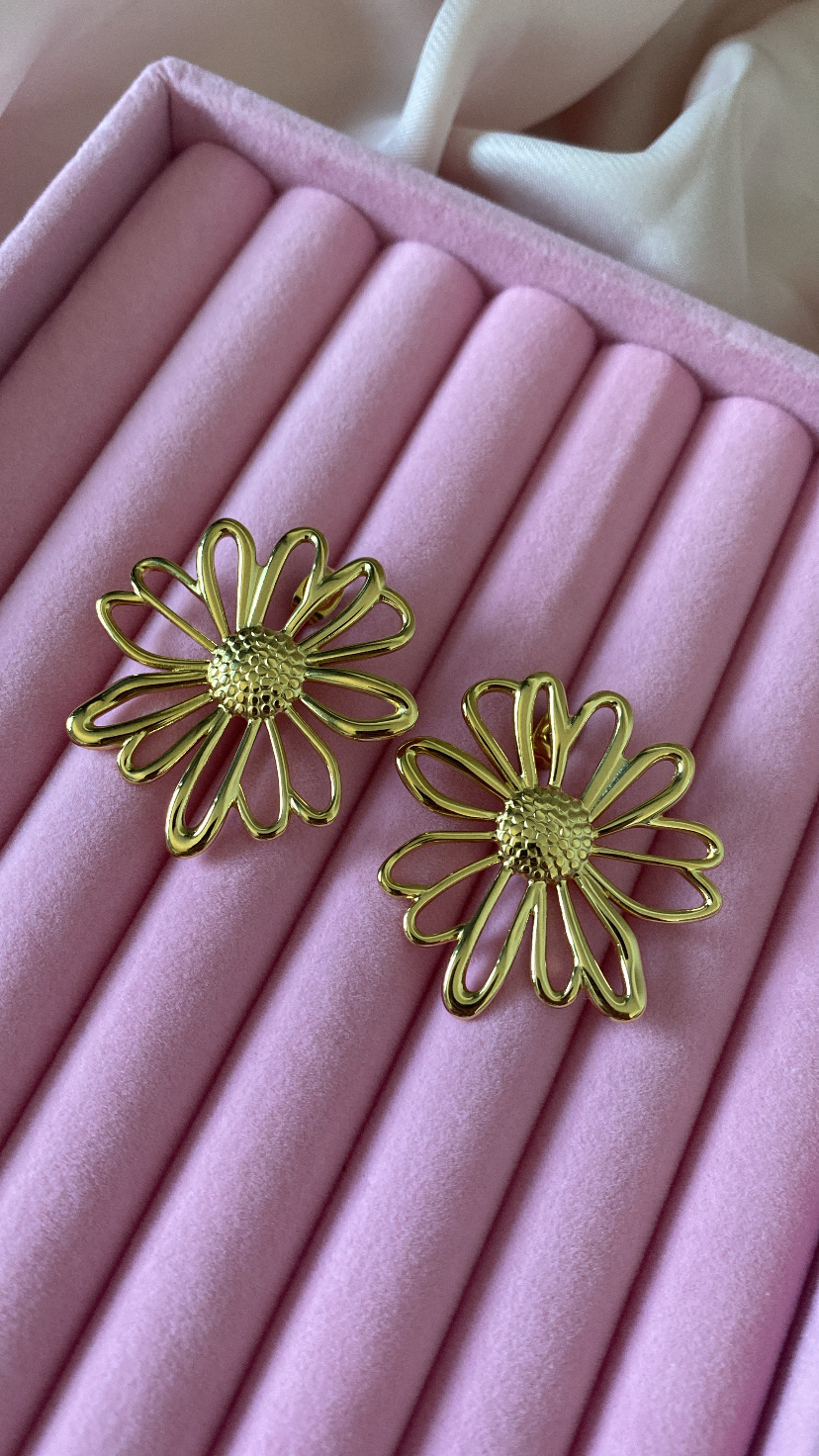 Brincos florais dourados sobre almofada rosa