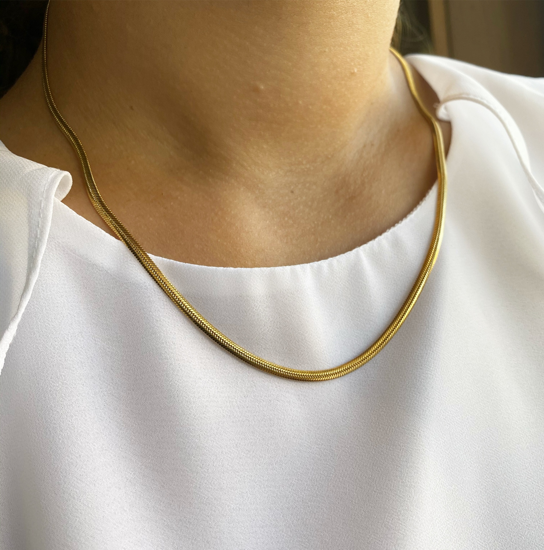 Colar dourado fino numa pessoa com blusa branca