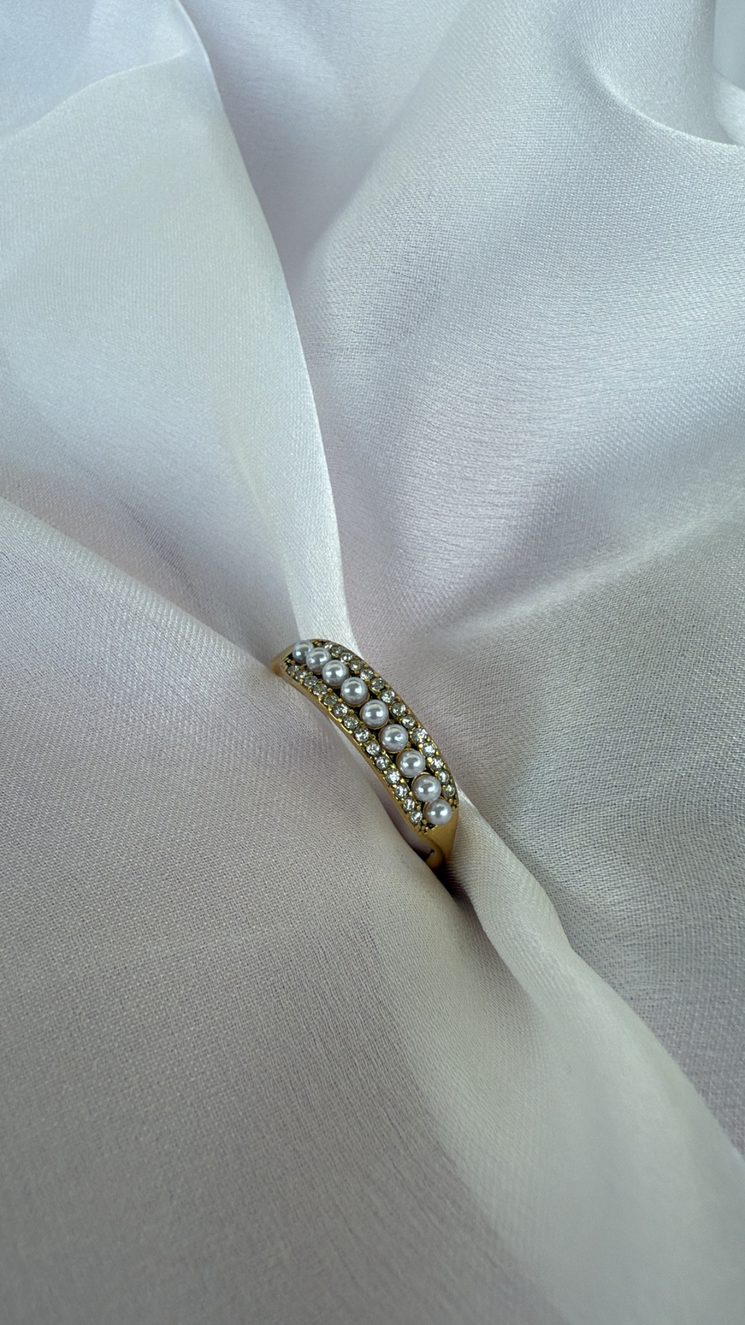 Anel dourado com pérolas e cristais sobre tecido branco