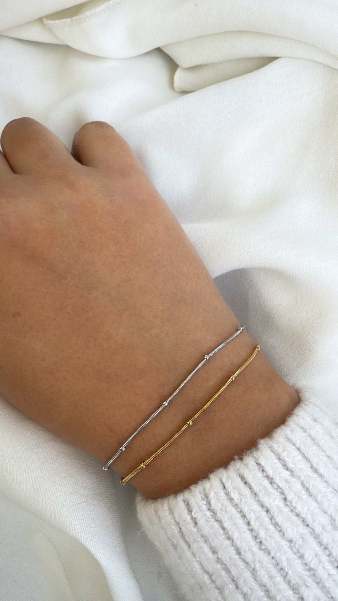 Pulseiras finas em tom prata e dourado no pulso com camisola branca de malha.