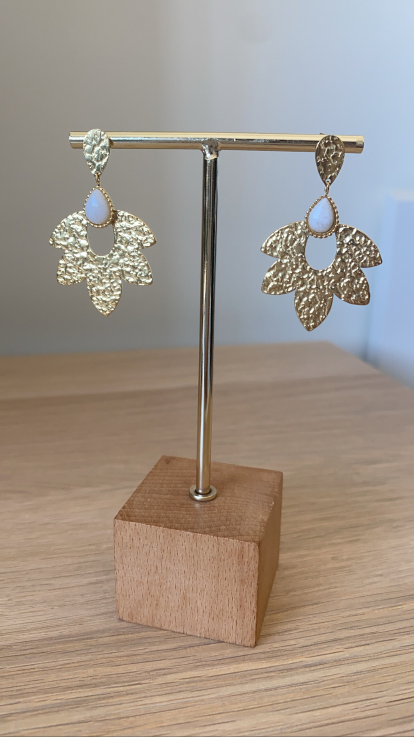 Brincos dourados com pedra branca pendurados em suporte de madeira