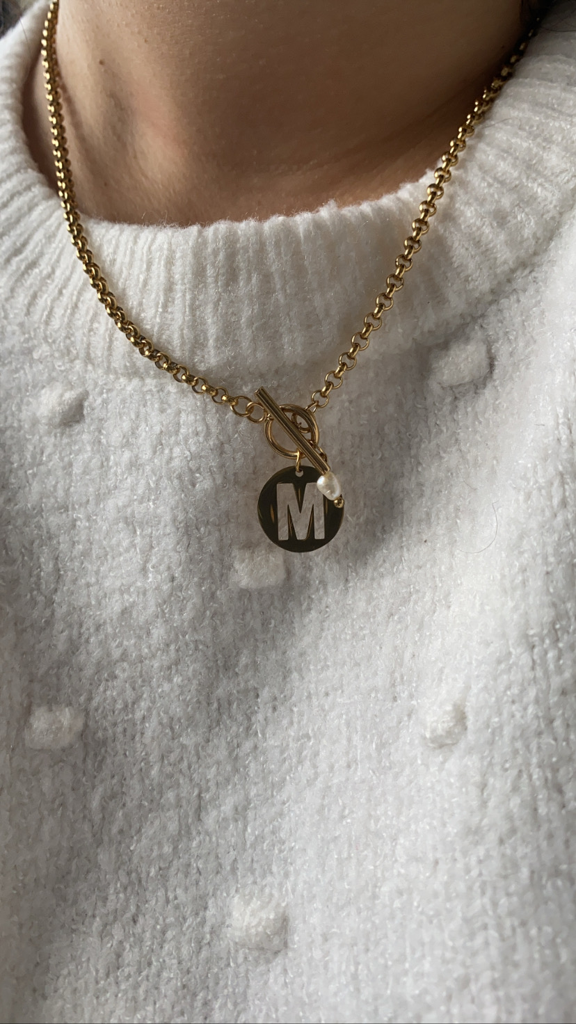 Colar dourado com pendente letra M e suéter branco com textura