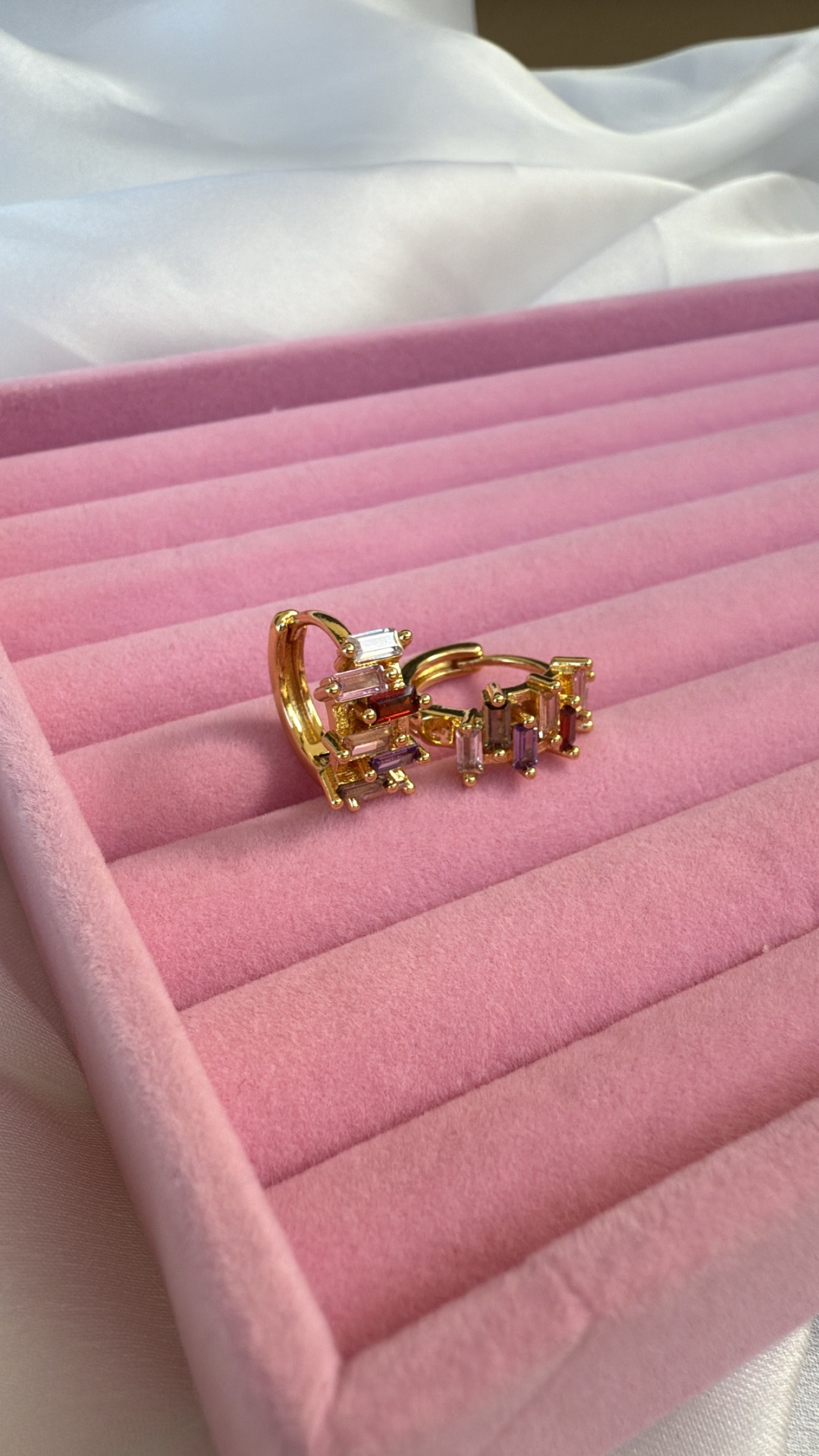 Brincos dourados com pedras transparentes numa caixa de veludo cor-de-rosa