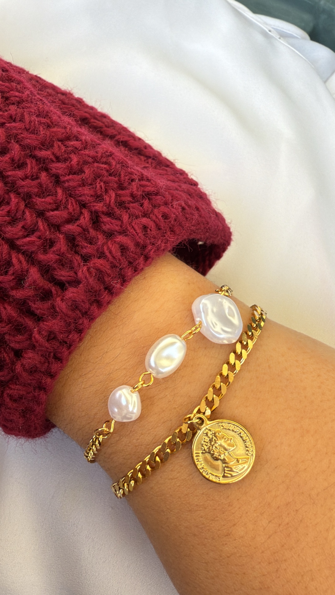 Pulseiras douradas com pérolas e pendente de moeda num pulso com camisola vermelha