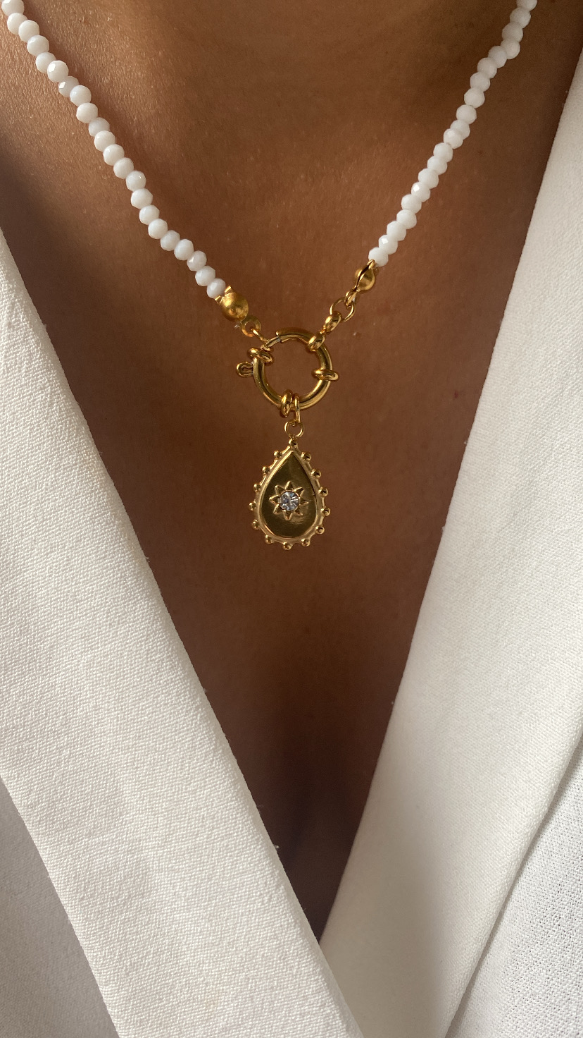 Colar de contas brancas com pingente dourado em gota e pedras brancas sobre roupa branca