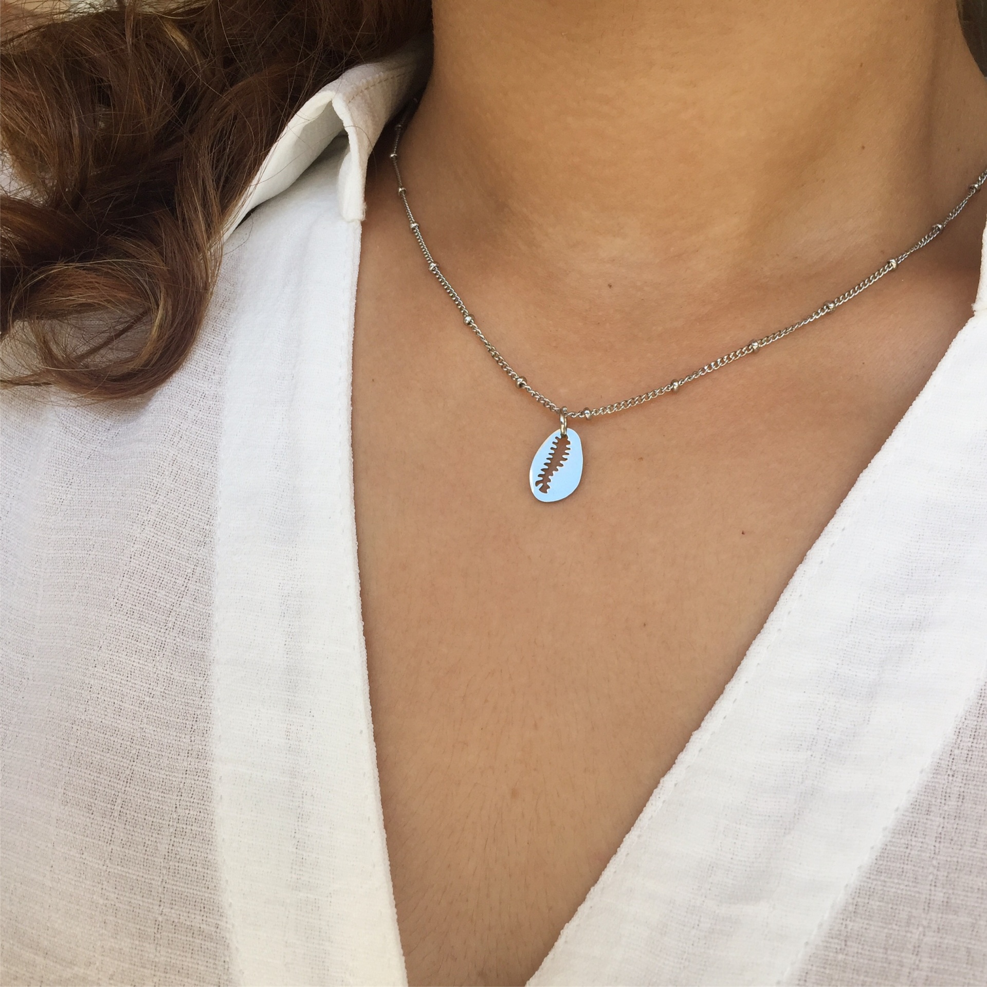 Colar prateado com pendente oval com desenho de folha usado com camisa branca