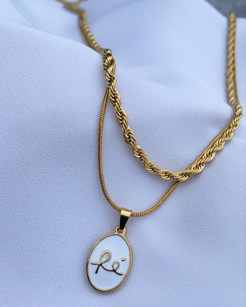 Colar dourado com pendente oval branco e assinatura dourada