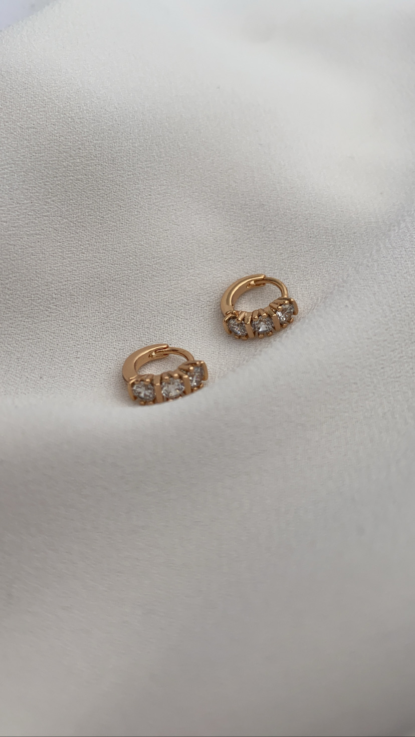 Brincos de ouro com três pedras brilhantes sobre tecido branco