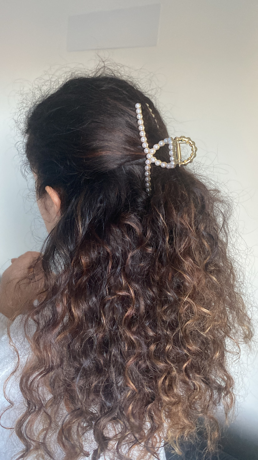 Presilha de cabelo de pérolas brancas com estrutura dourada em cabelo cacheado castanho