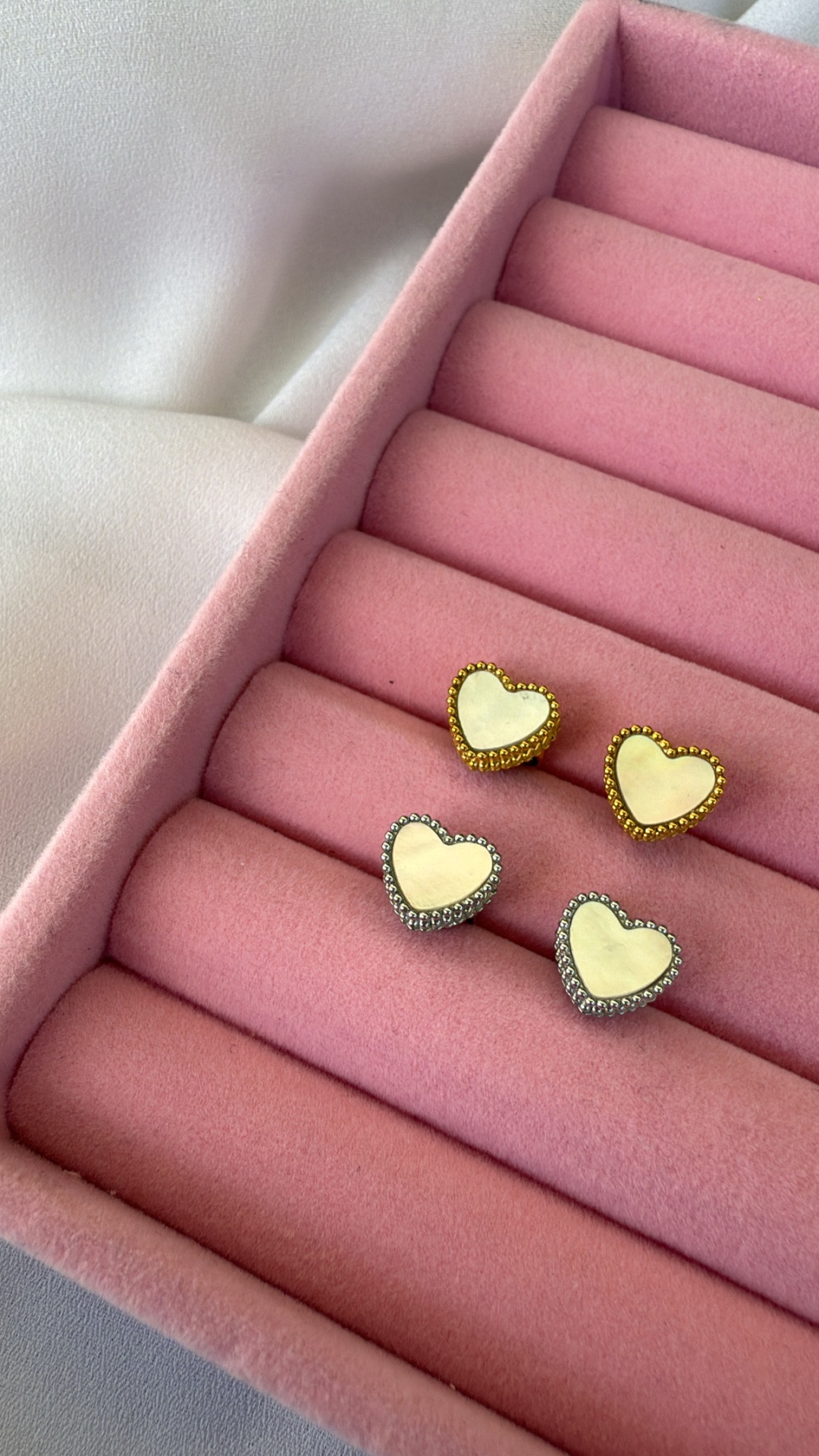 Brincos em forma de coração com molduras dourada e prateada numa caixa de veludo rosa