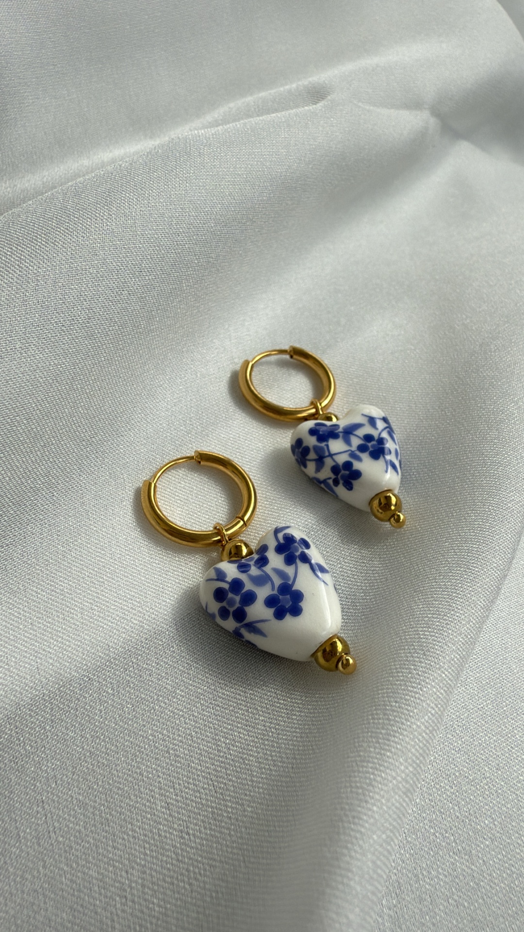 Brincos dourados com pendente de coração branco com padrão floral azul