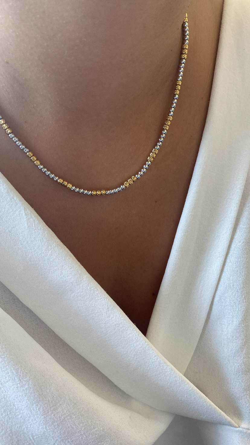 Colar delicado dourado e prateado sobre pele e roupa branca