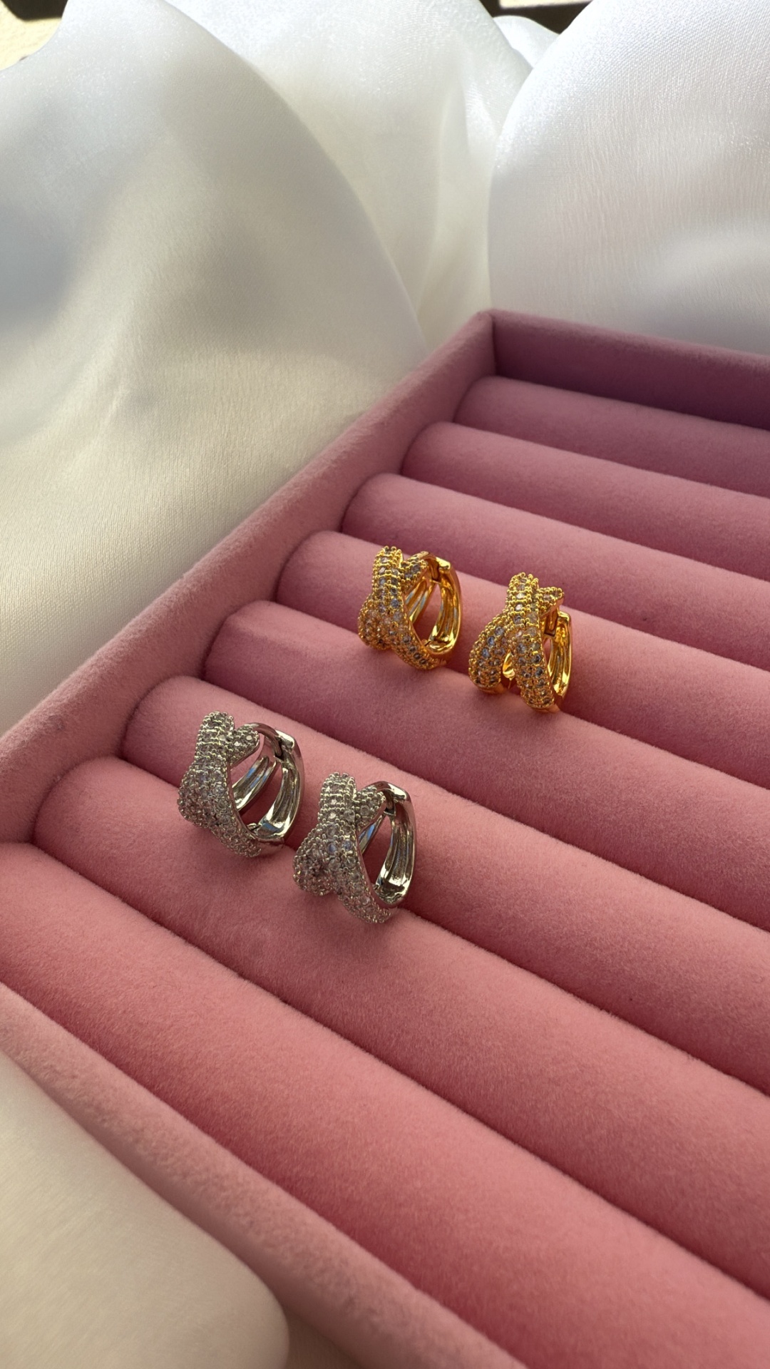 Dois pares de brincos brilhantes dourados e prateados numa caixa rosa de veludo