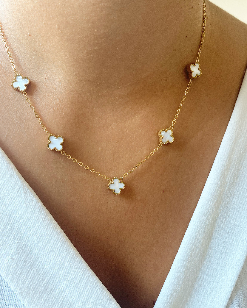 Colar com cinco flores brancas em corrente dourada, usado sobre pele clara.