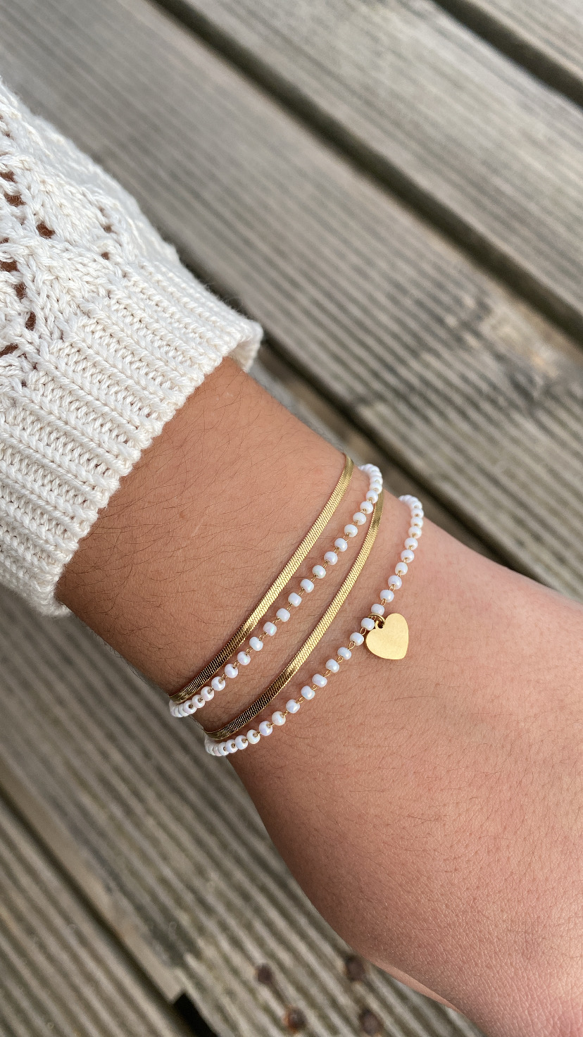 Pulseiras douradas e brancas no pulso com pendente de coração