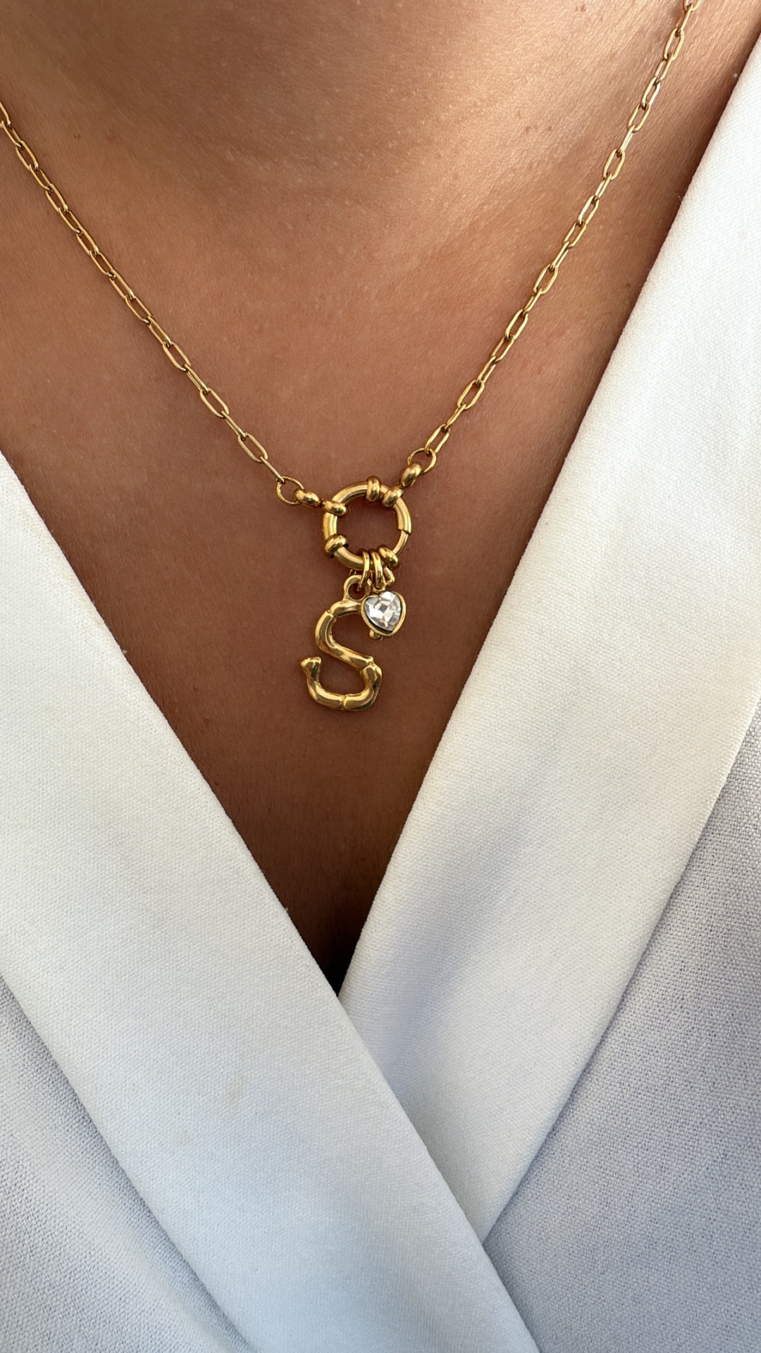 Colar dourado com pendente letra S e coração de pedra sobre roupa branca
