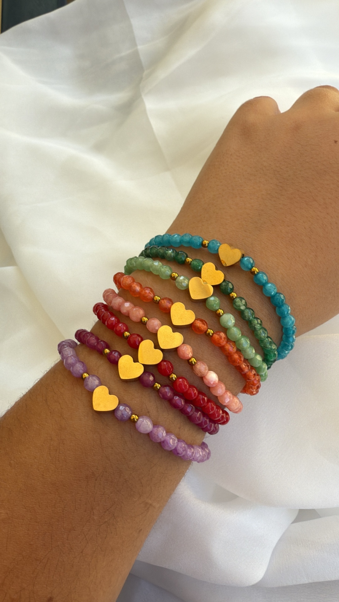 Pulseiras coloridas com corações dourados num pulso sobre tecido branco