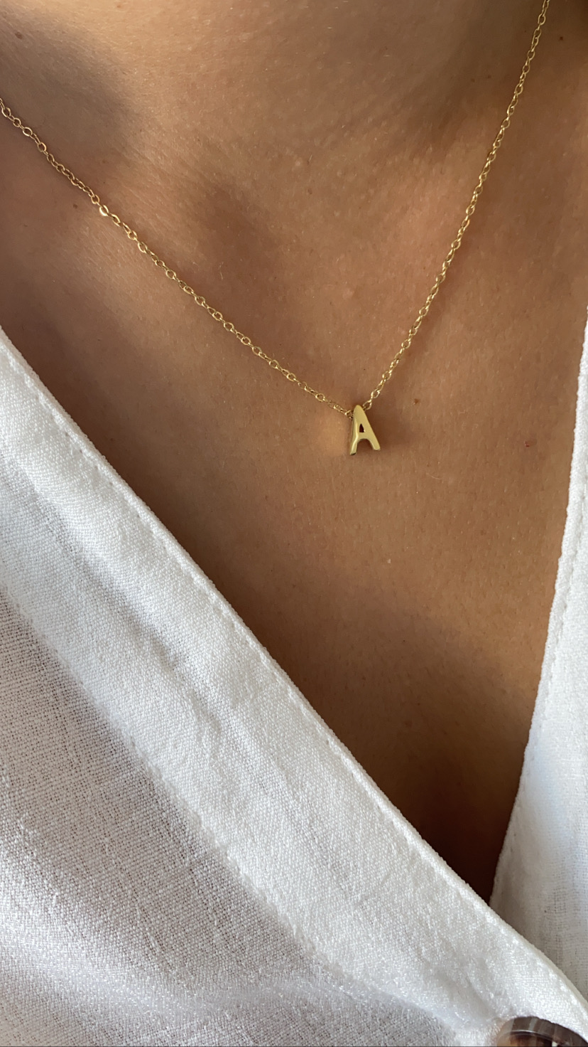 Colar dourado com pendente letra A no pescoço com blusa branca