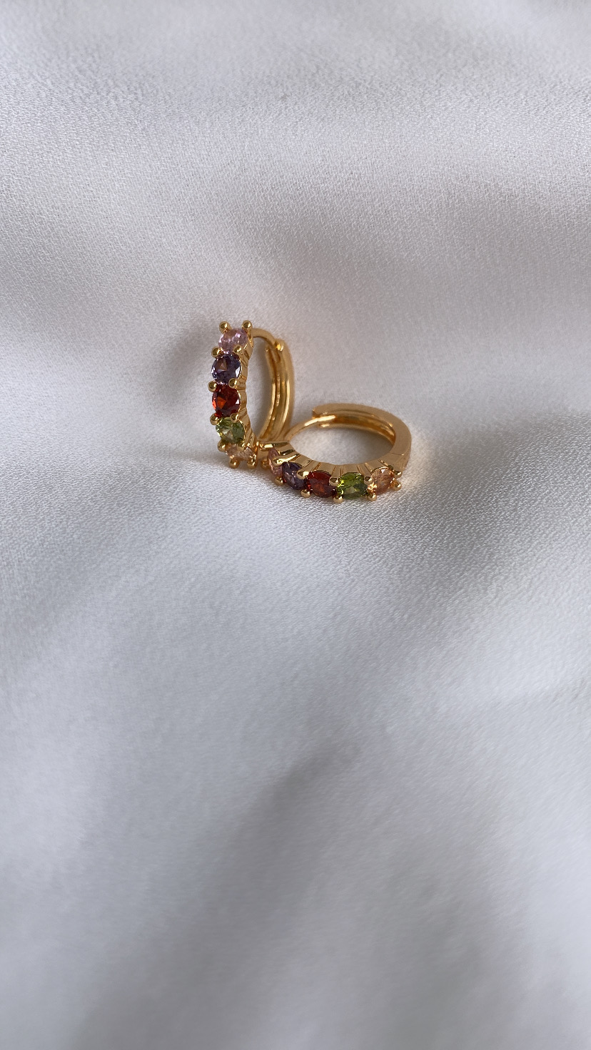 Brincos dourados em argola com pedras coloridas sobre tecido branco