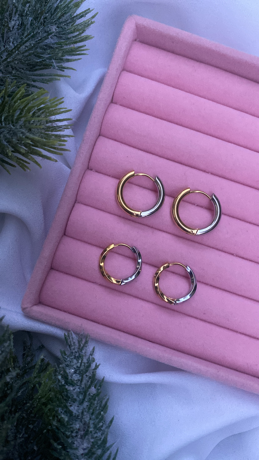 Dois pares de brincos de argola bicolores em caixa de veludo rosa com elementos naturais ao lado