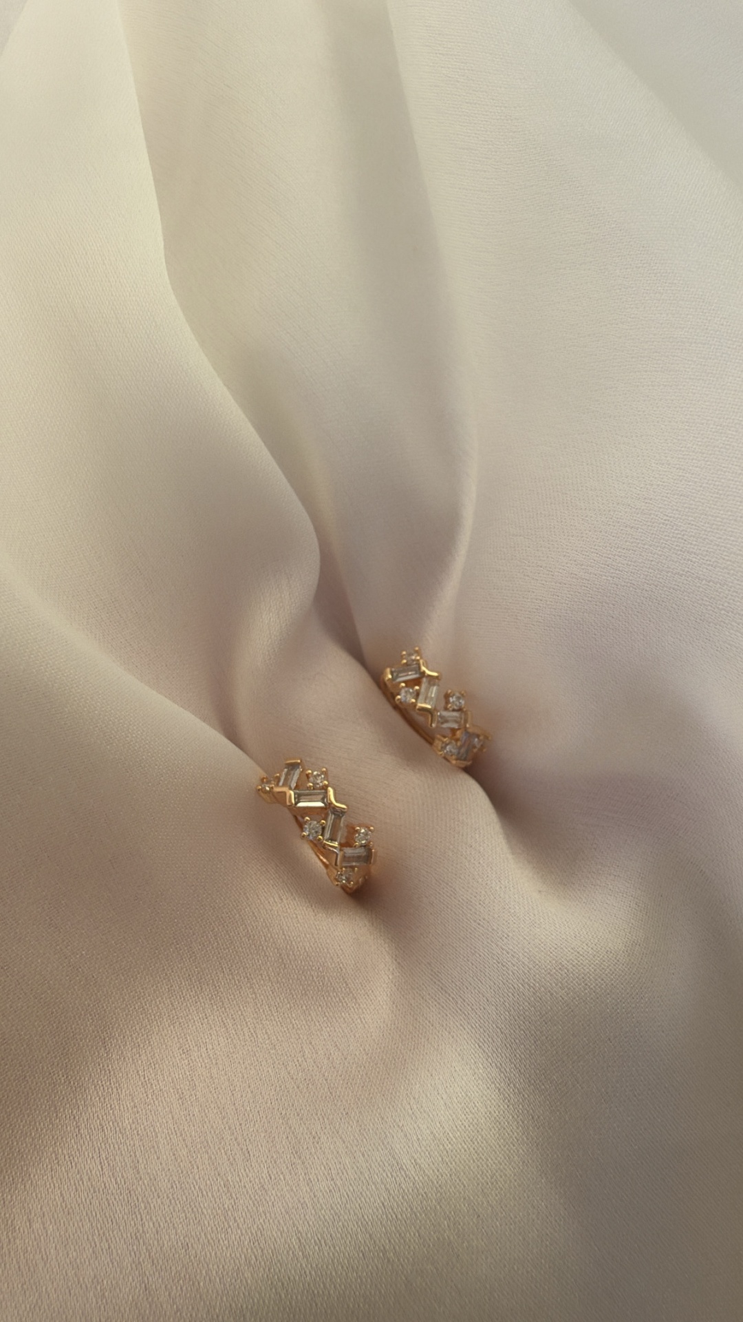 Brincos dourados com pedras transparentes sobre tecido branco