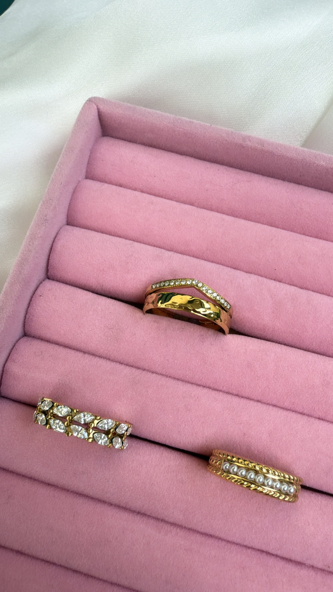 Três anéis dourados numa caixa de veludo rosa, com pedras e pérolas