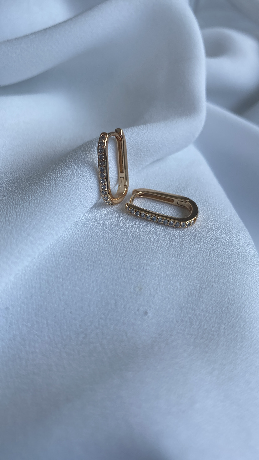 Par de brincos dourados com pedras sobre tecido branco