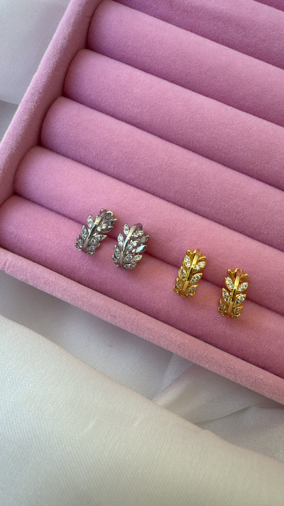 Dois pares de brincos em formato de folhas, prateado e dourado, com pedras, caixa de veludo rosa
