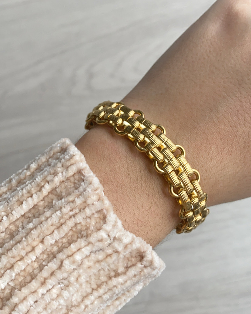 Pulseira dourada entrelaçada no pulso com camisola creme texturada