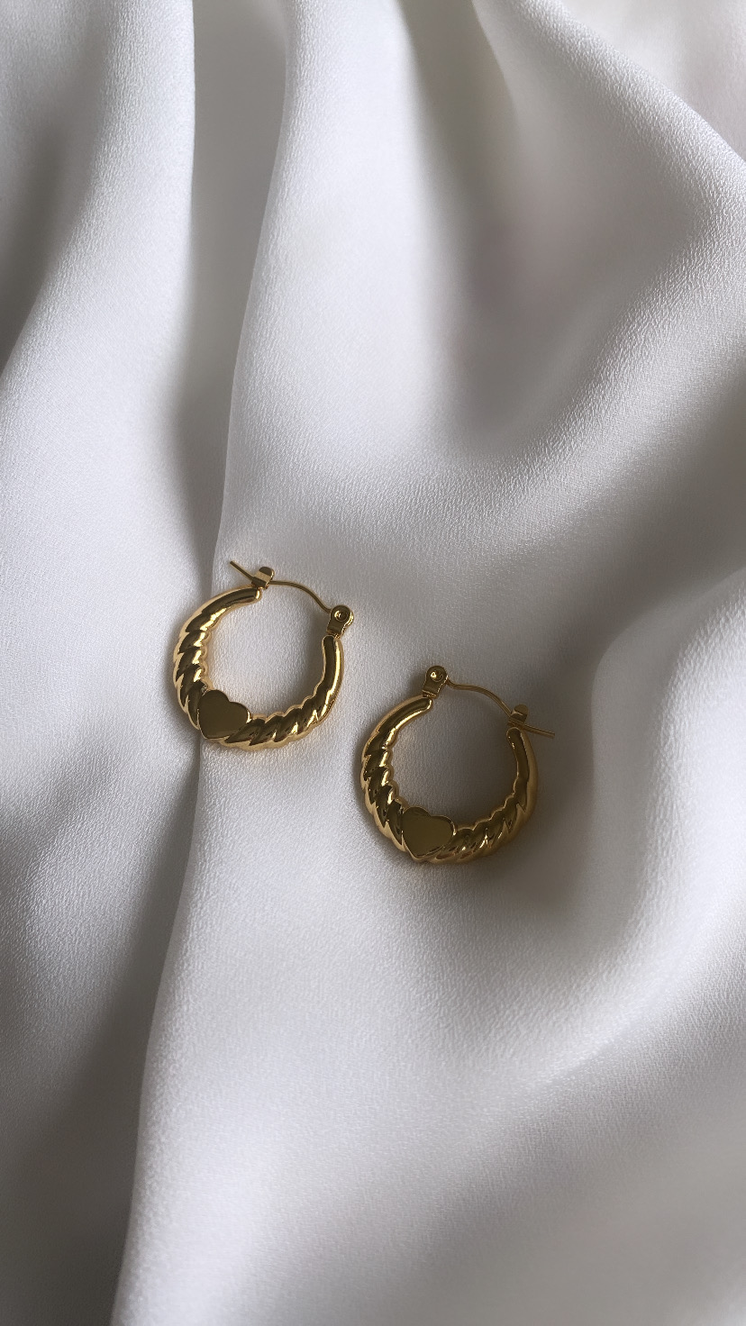 Brincos de argola dourados com padrão e coração sobre tecido branco