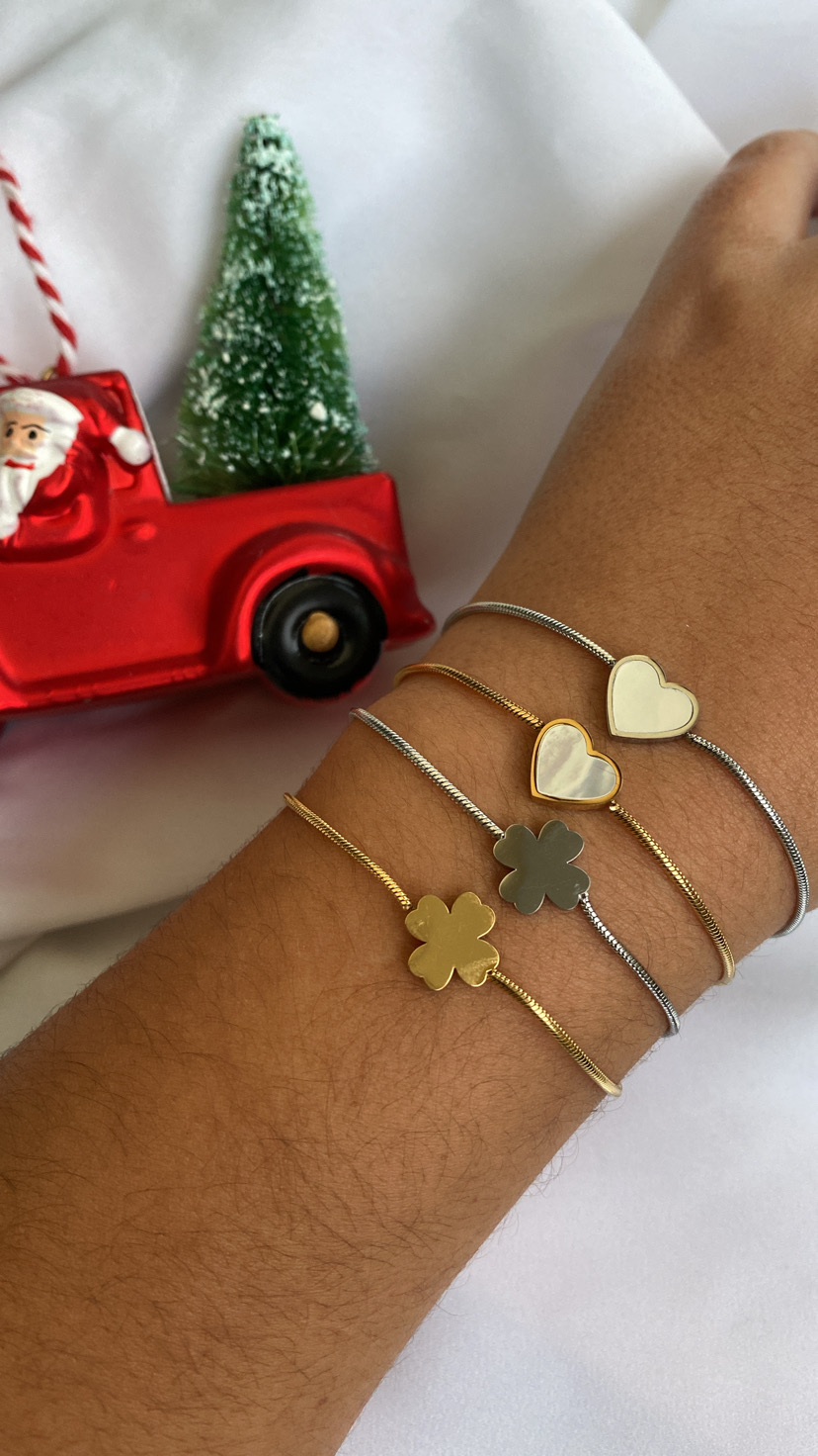Pulseras douradas e prateadas com pendentes de coração e trevo num pulso junto de decoração natalícia