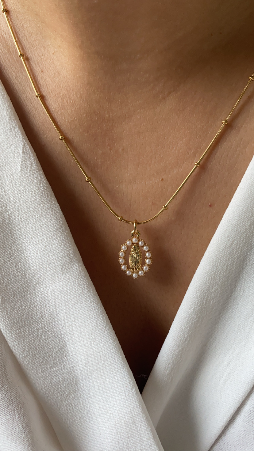 Colar dourado com pendente oval e pérolas brancas colocado sobre roupa branca