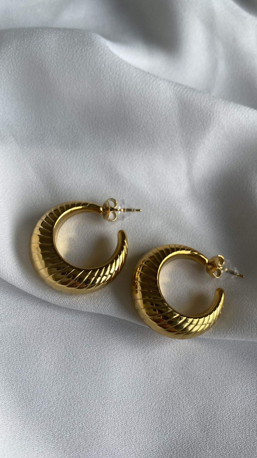 Brincos dourados em argola com textura sobre tecido branco