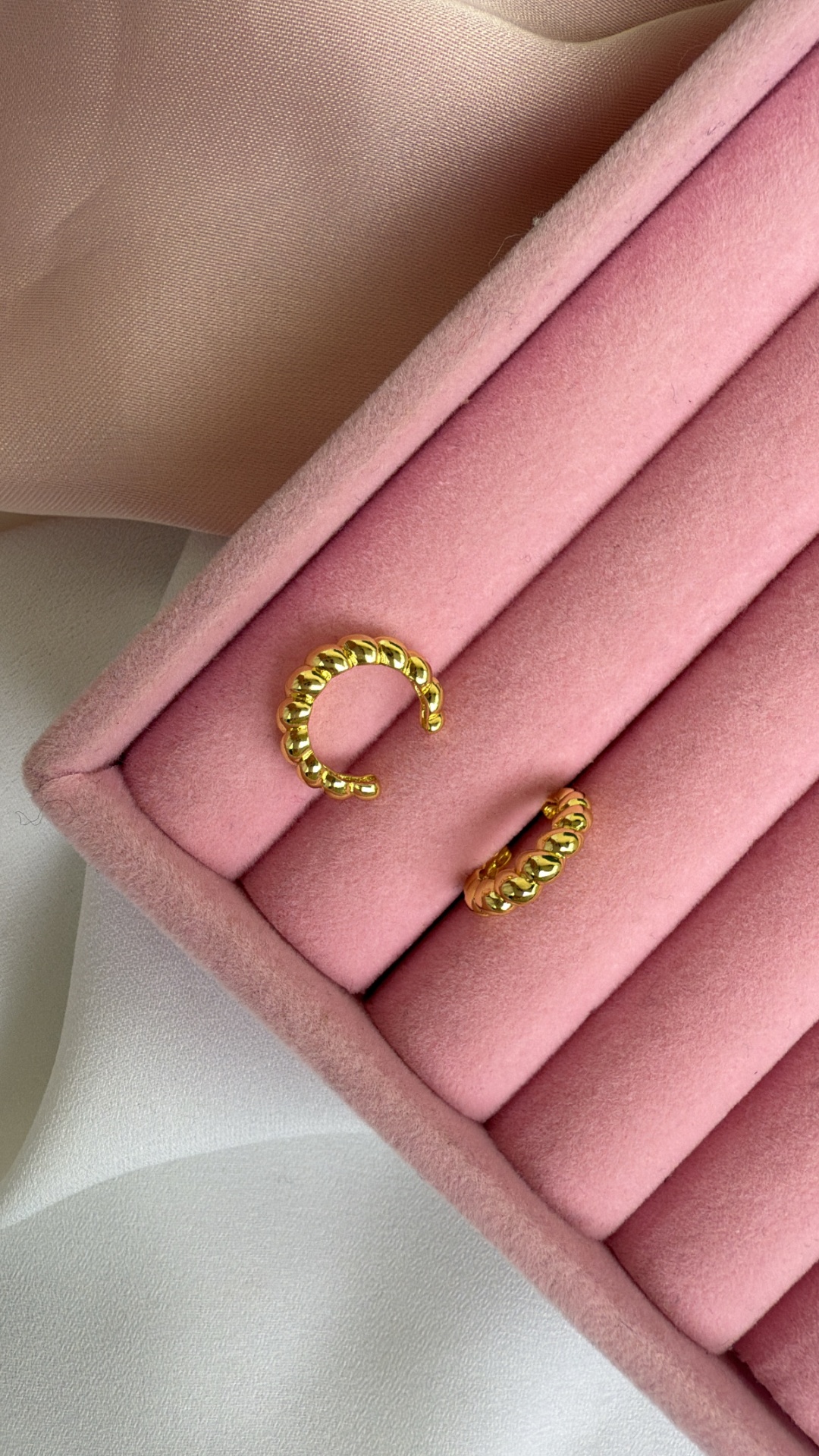 Brincos dourados texturizados numa caixa de veludo rosa