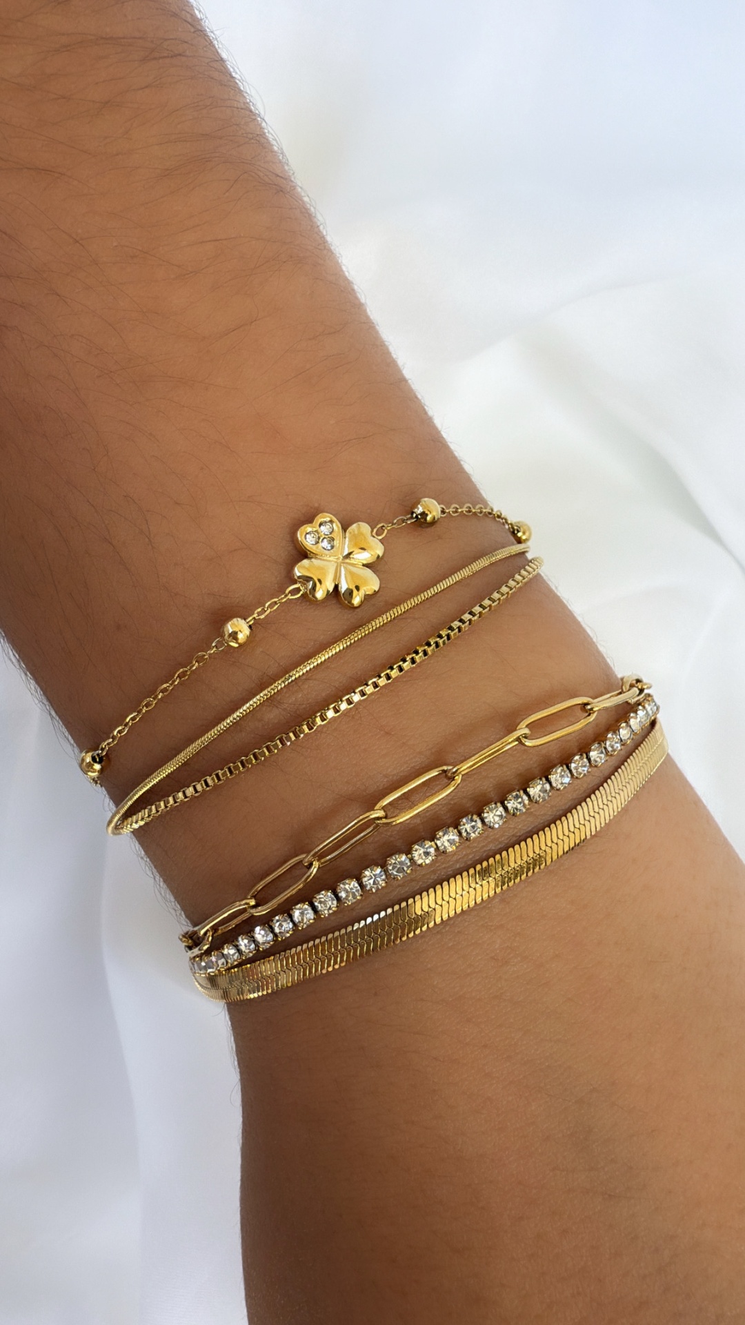 Conjunto de seis pulseiras douradas com diferentes estilos no braço sobre fundo branco