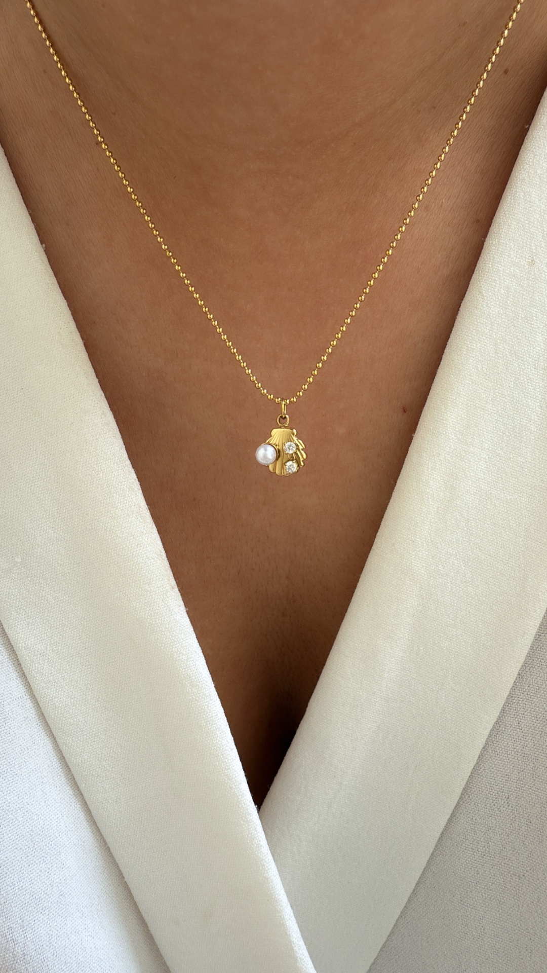 Colar dourado com pendente em forma de mão com pedras