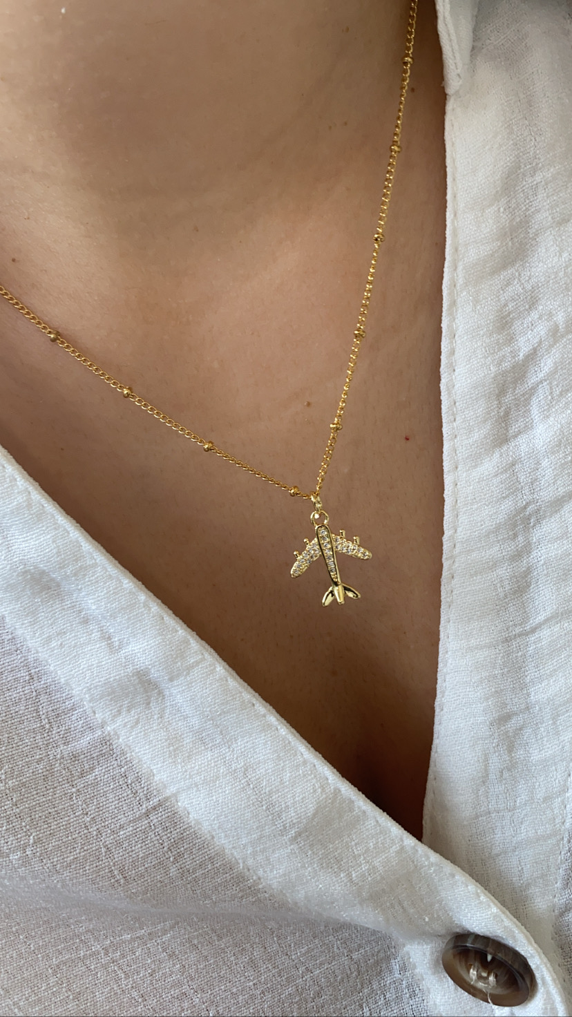 colar dourado com pendente de avião e camisa branca