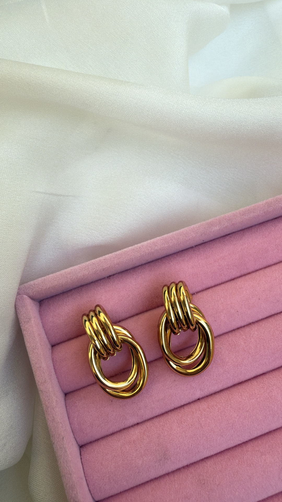 Brincos dourados em caixa de veludo rosa sobre tecido branco