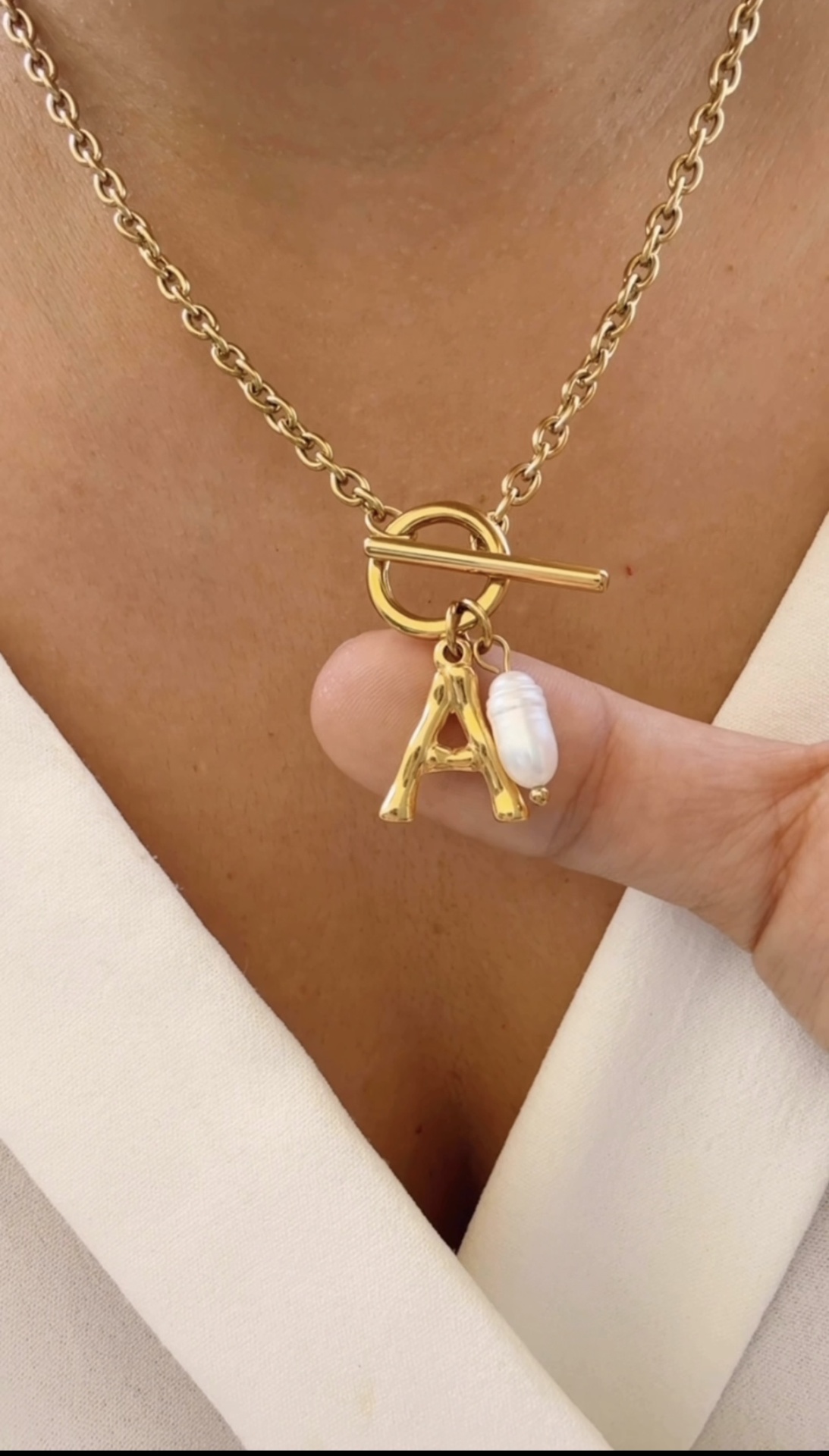 Colar dourado com pendente letra A e pérola em pescoço