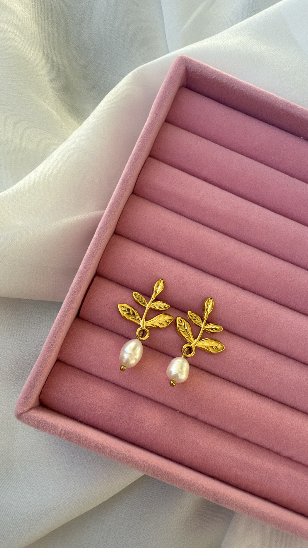 Brincos dourados com pérolas em caixa rosa sobre tecido branco