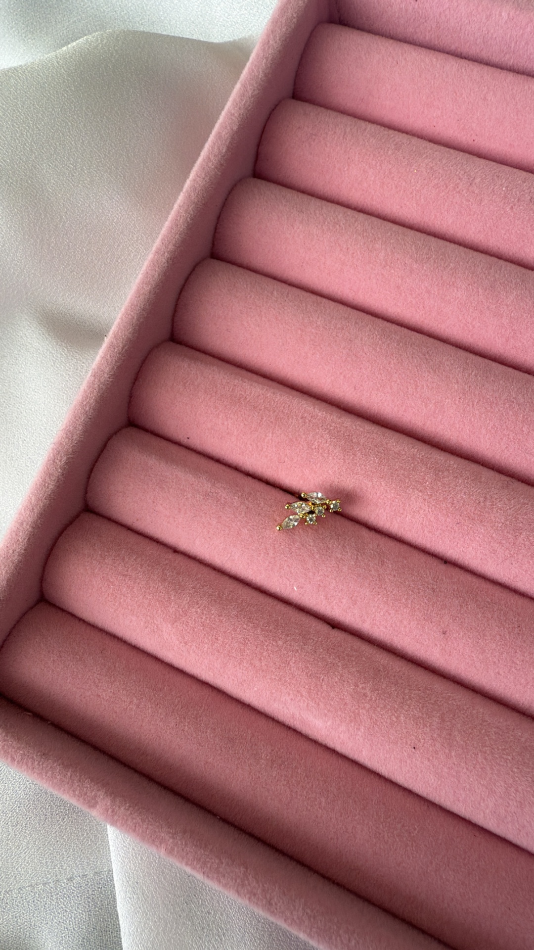 Pequena joia dourada com pedras sobre almofada rosa