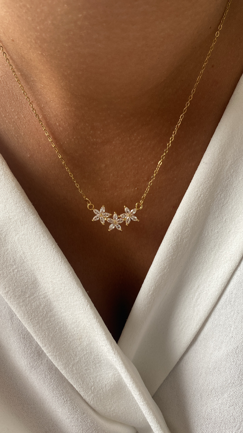 Colar dourado com três flores prateadas e brilhantes no pescoço