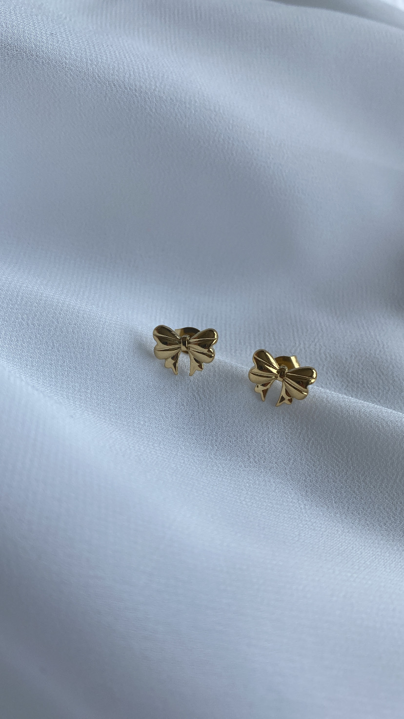 Par de brincos em formato de laço dourados sobre fundo branco