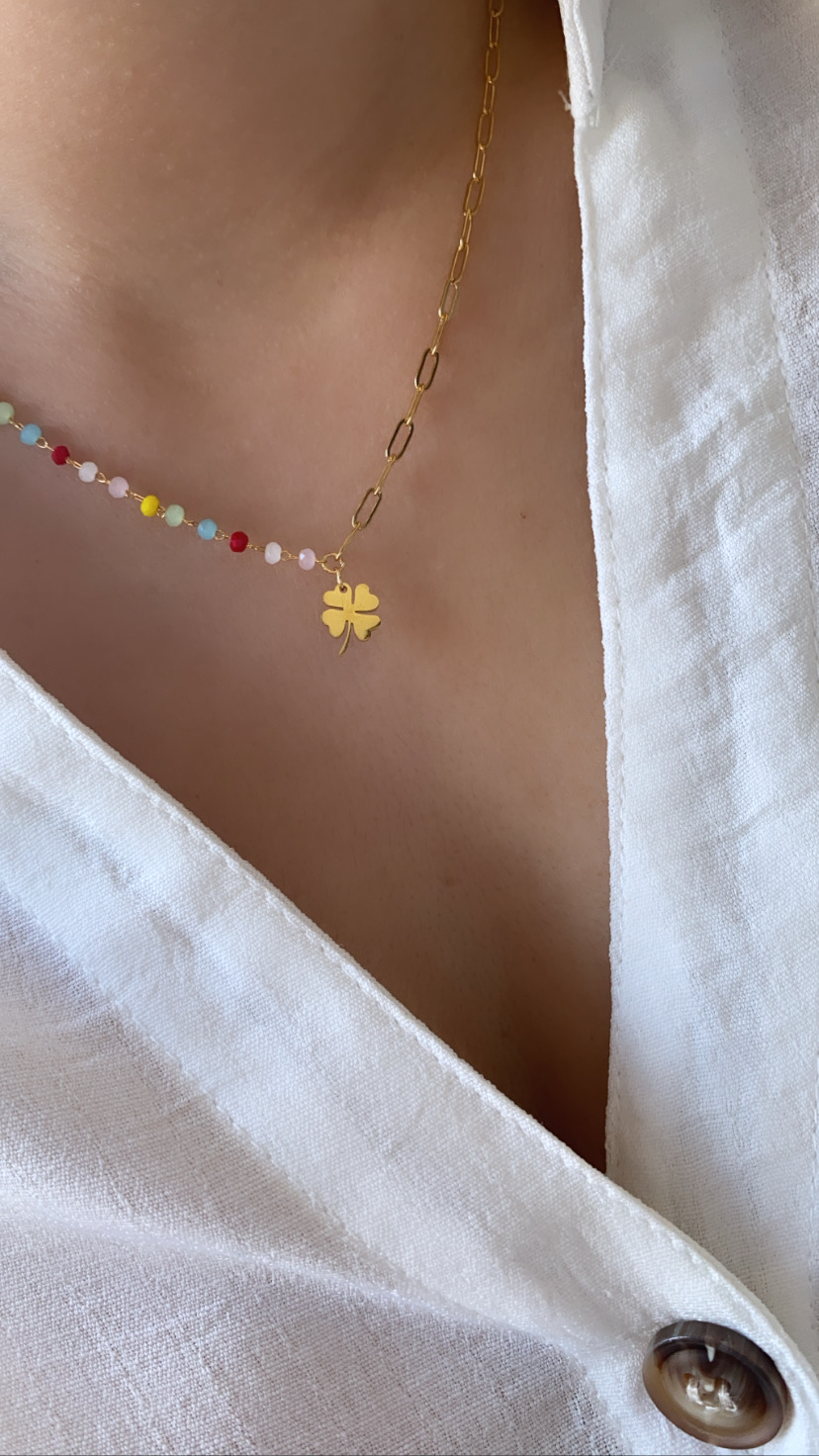 Colar dourado com pendente de trevo e cristais coloridos numa pessoa com camisa branca