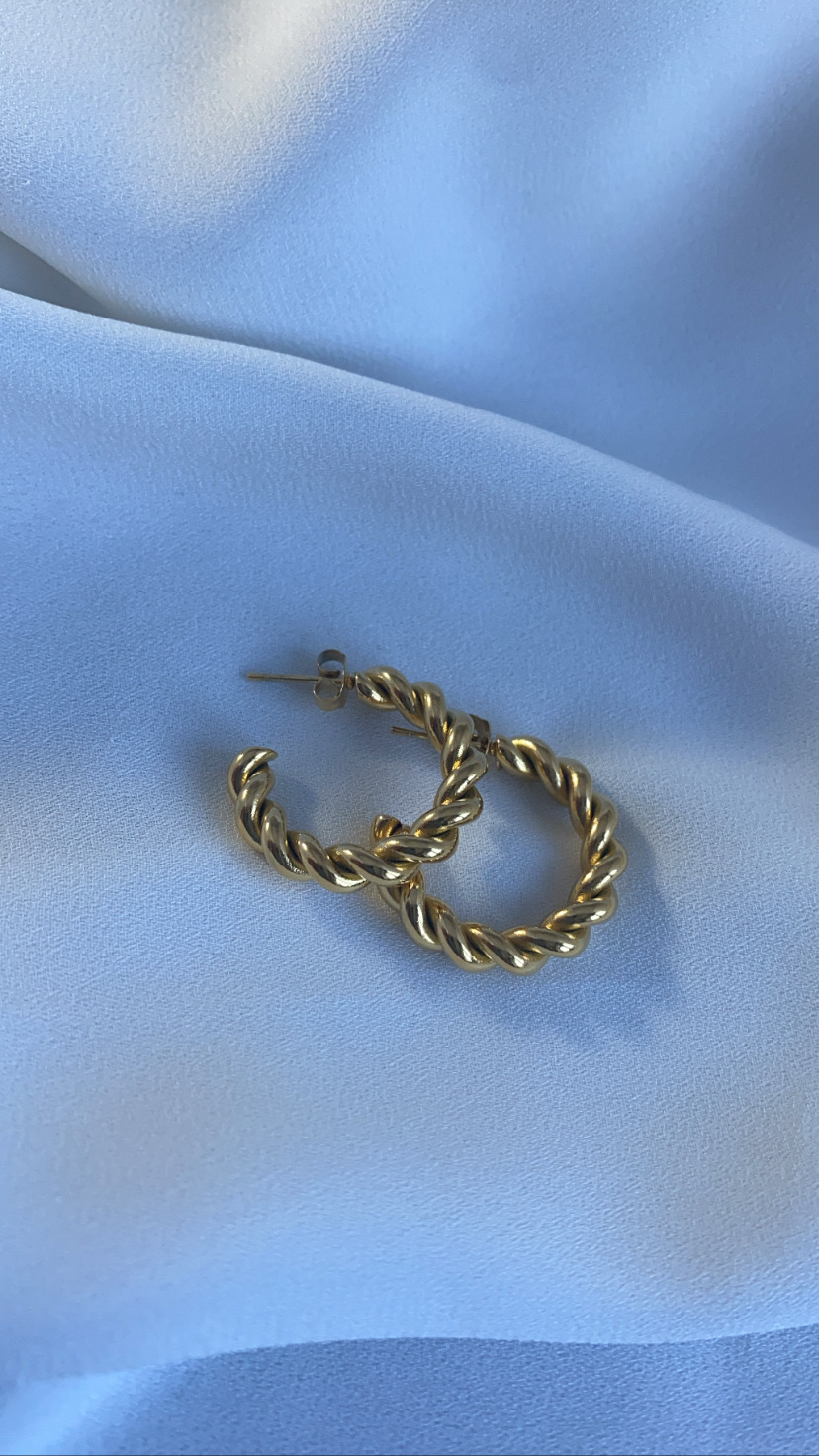 Brincos dourados em argola torcido sobre tecido azul claro